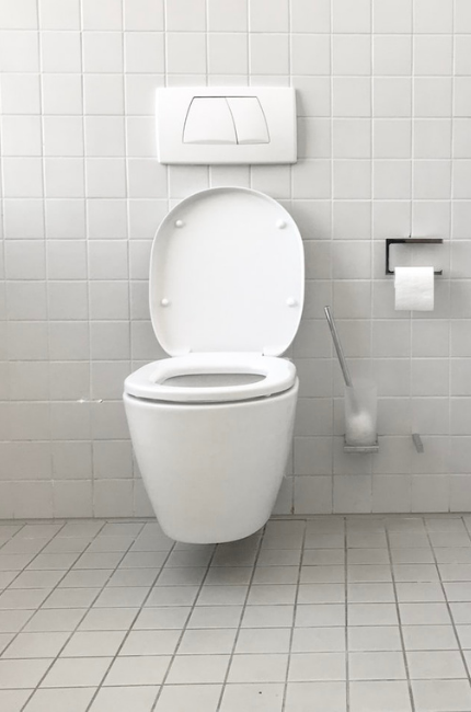 Na środku ściany w łazience znajduje się toaleta. Toaleta ma zapchany odpływ. Powyzej znajduje się spłuczka a po boku papier toaletowy.